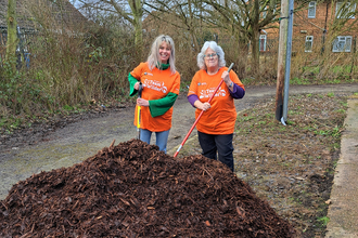 Two people from FoAK digging a pile of woodchip
